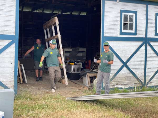 The Recyclers crew carrying a wooden ladder and debris out of a barn during a property cleanup