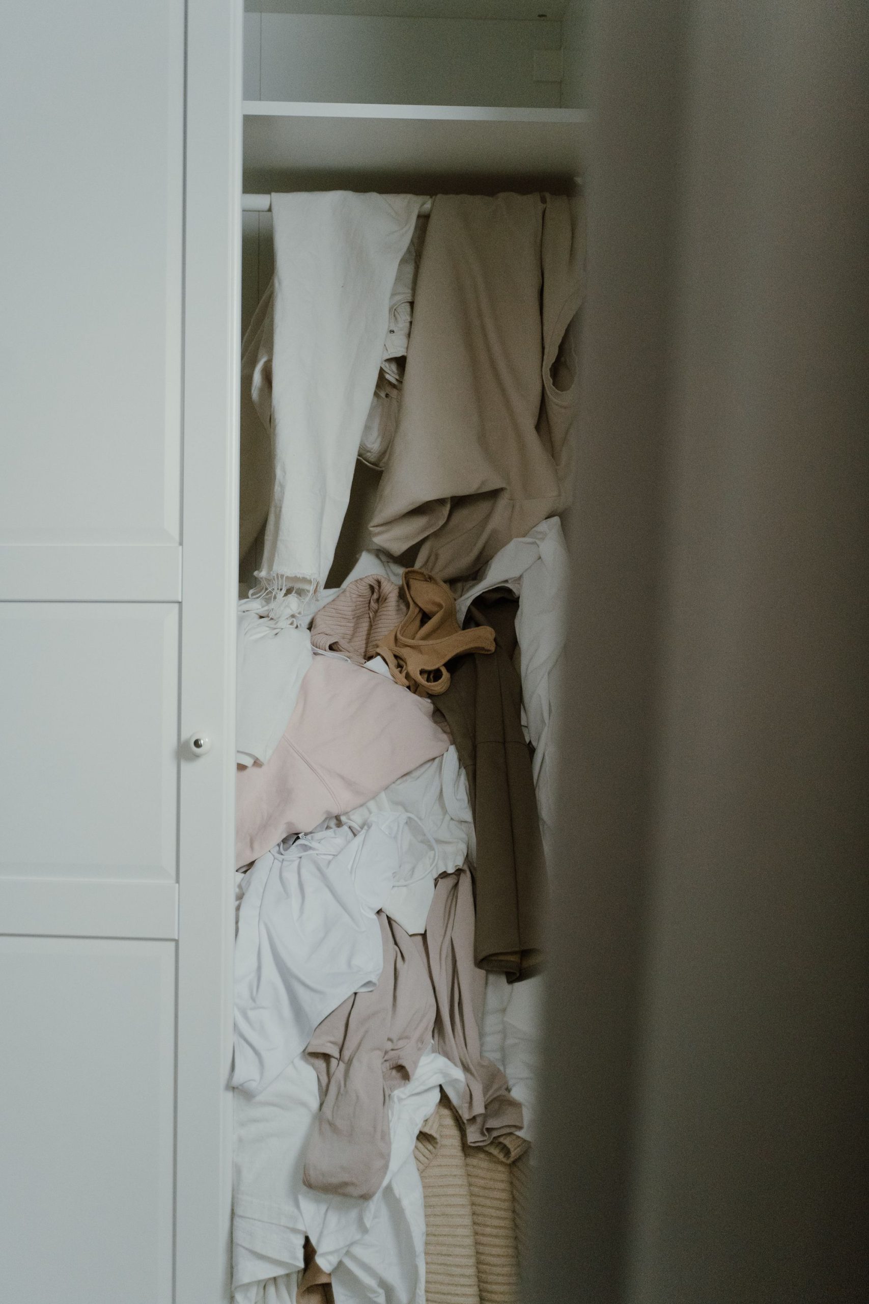 A crowded closet with clothes piled and hanging from the shelves