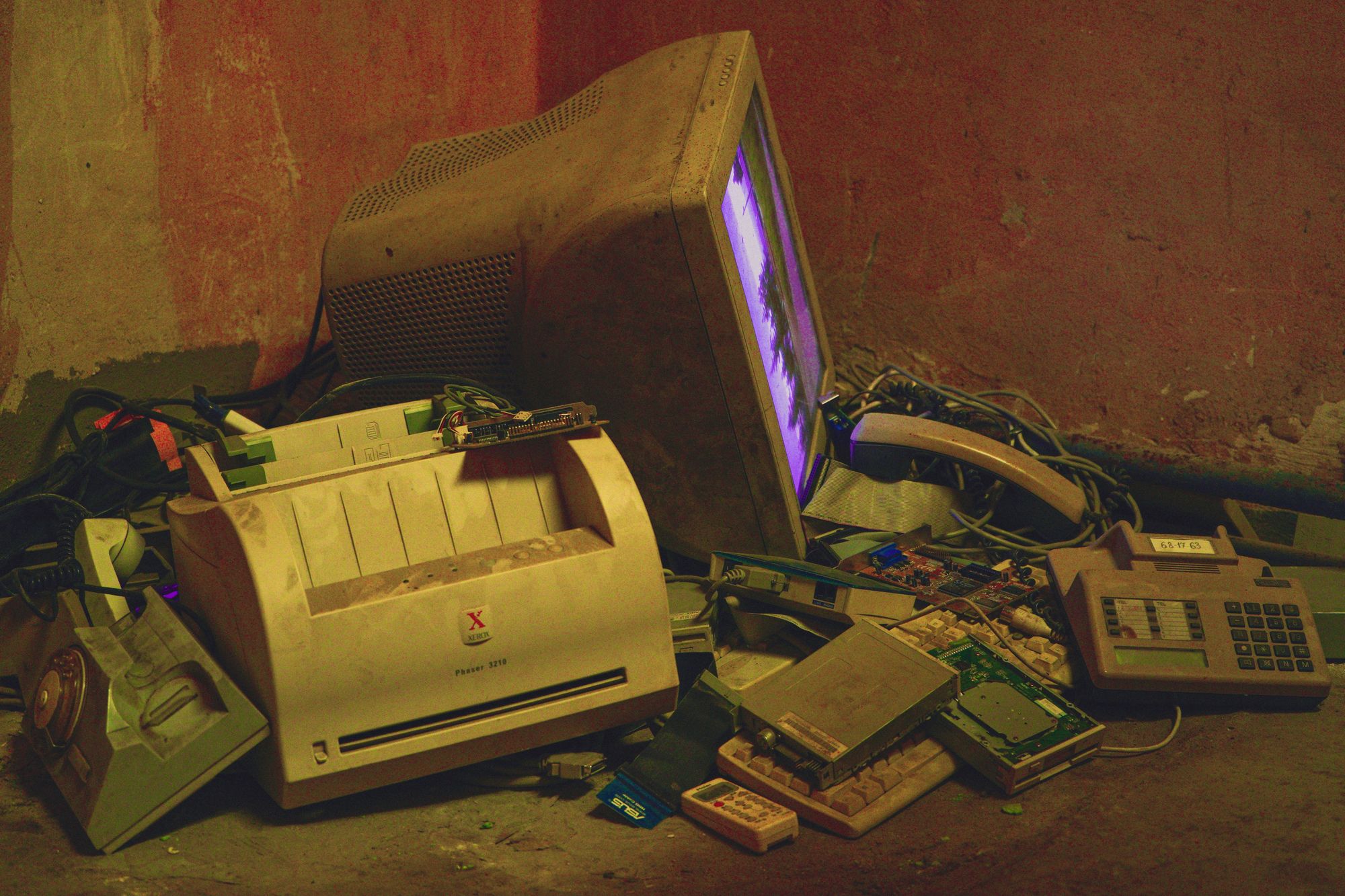 An old printer, computer monitor and phones piled in a basement