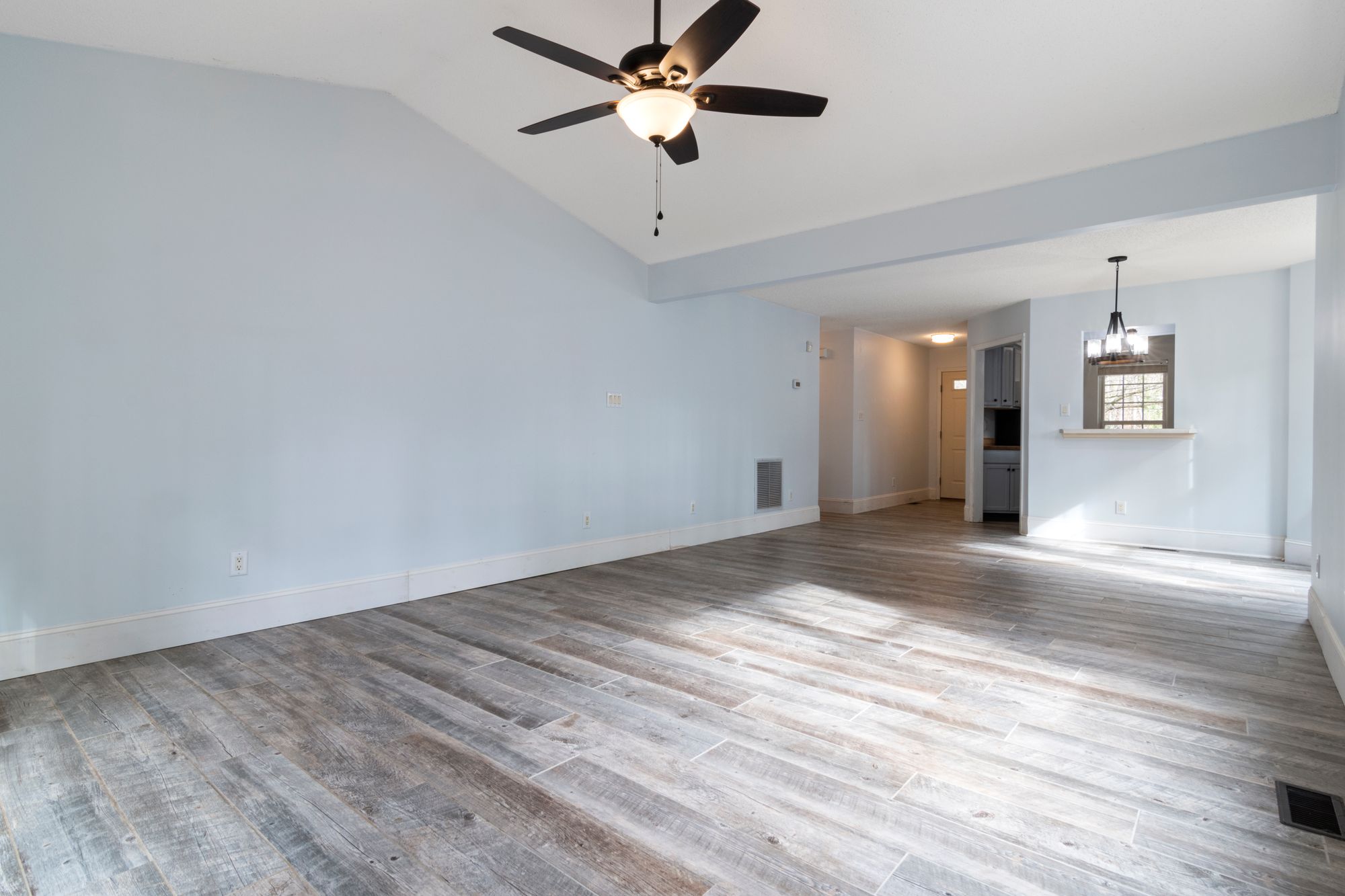 An empty apartment with gray wood floors and a ceiling fan